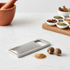 Small stainless steel grater on a white marble counter with nutmeg