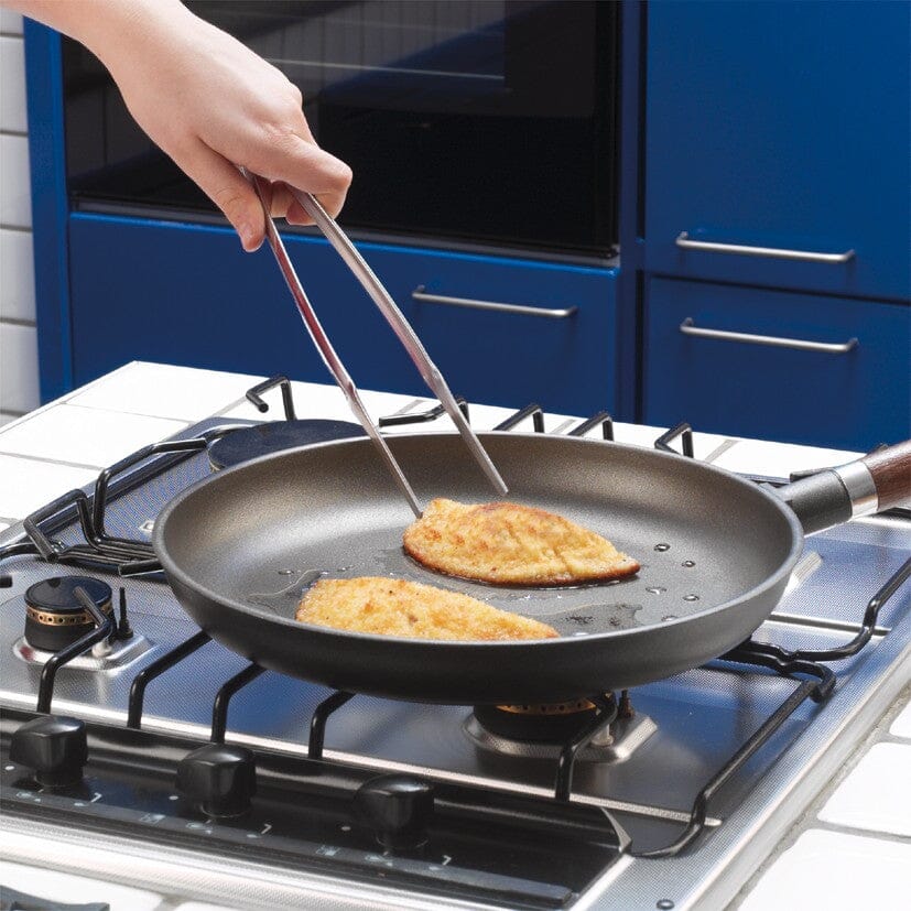 Person using stainless steel chef tongs with a frying pan in a blue kitchen