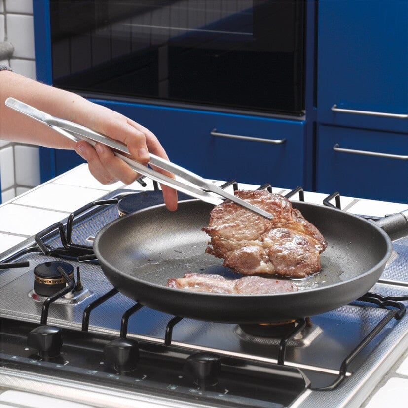 Person using stainless steel chef tongs with a frying pan in a blue kitchen