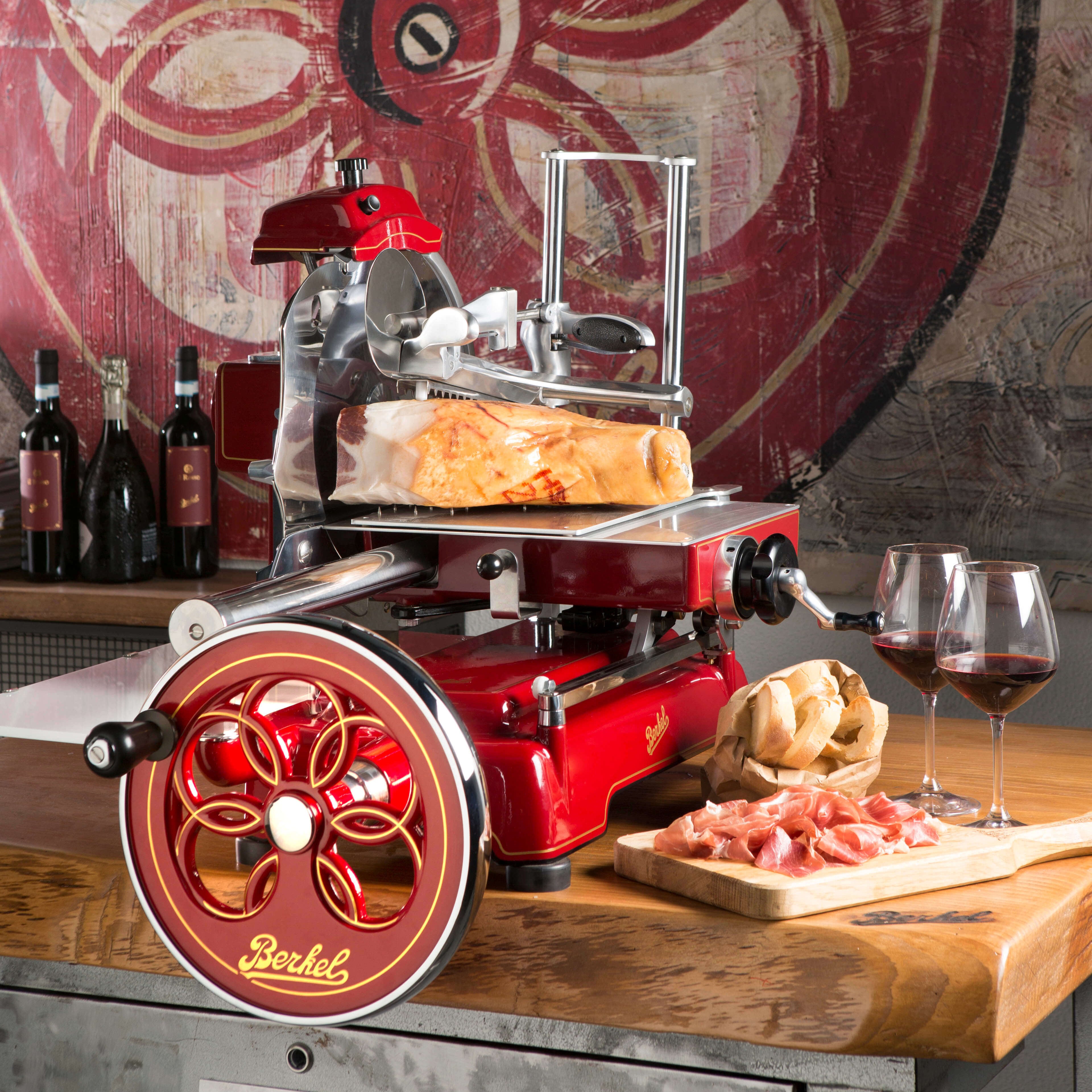 Berkel Volano B3 flywheel slicer on a countertop in a rustic kitchen, alongside win, prosciutto and bread.