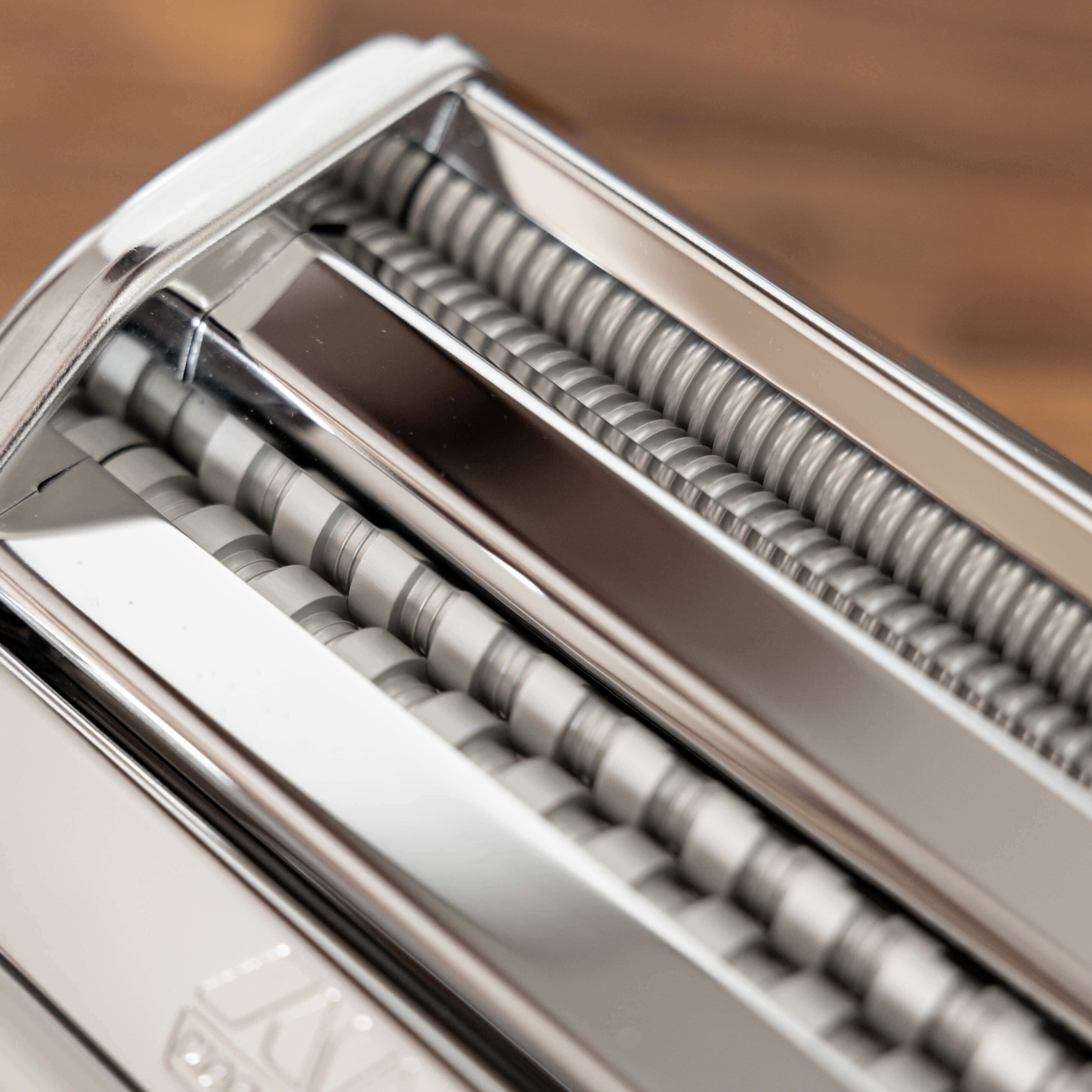 Close-up of a pasta maker with metal rollers on a wooden surface