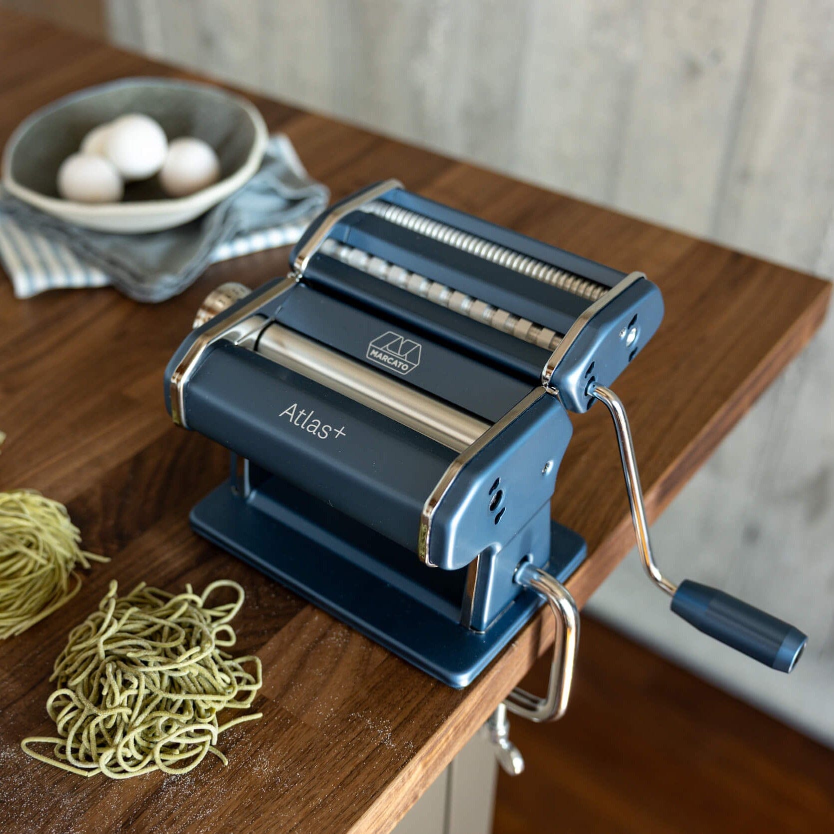 Pasta maker on a wooden table with fresh pasta strands
