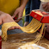 Red Marcato atlas+ pasta maker being used to make fresh pasta on a wooden surface