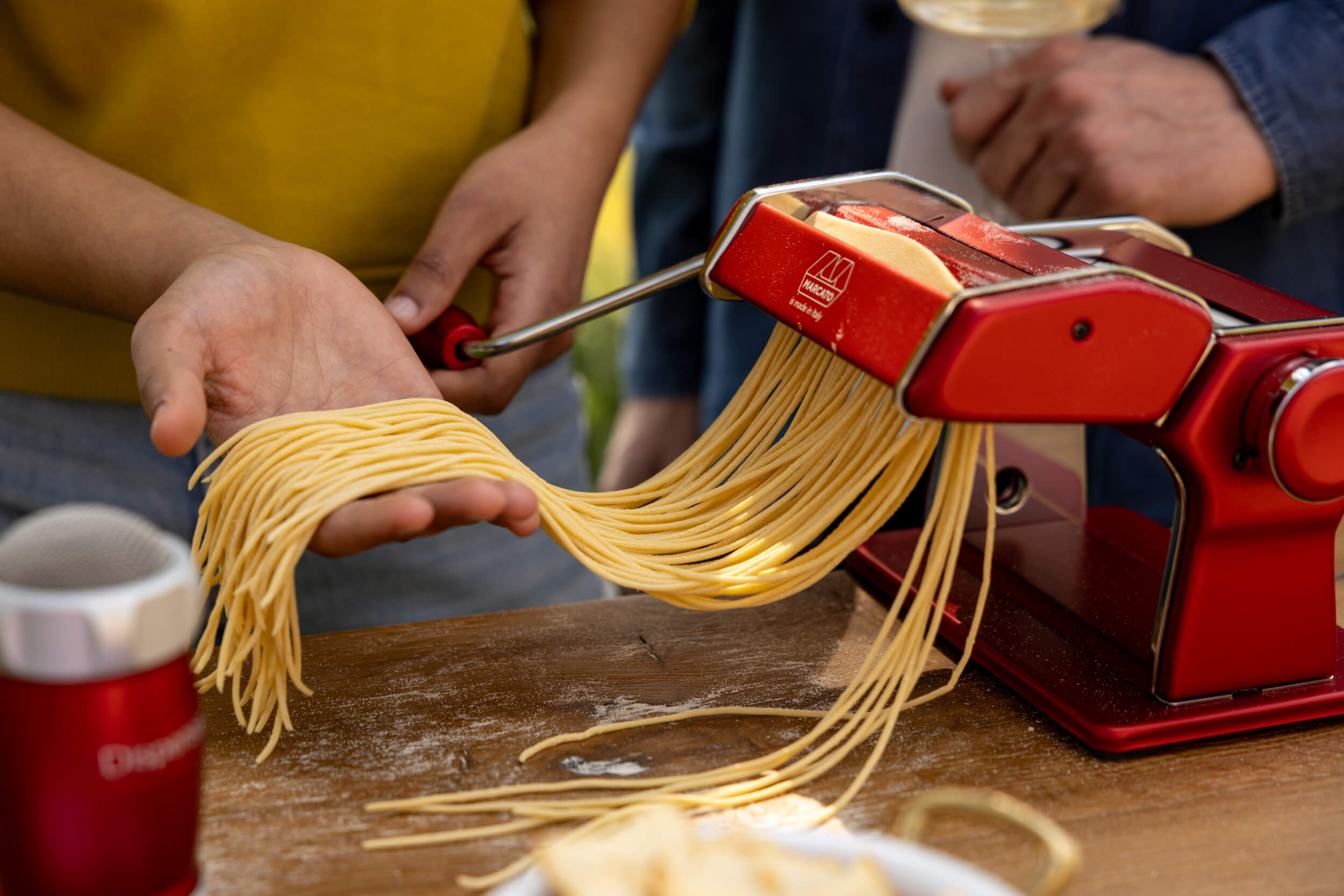 Red Marcato pasta maker with fresh pasta being pulled out on a wooden table.
