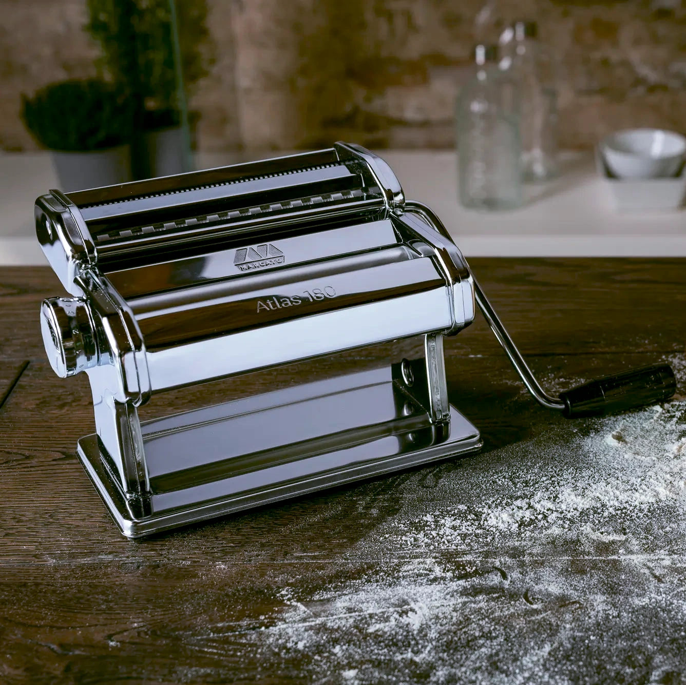 Marcato Atlas 180 pasta maker on a wooden table with flour, rustic kitchen setting.
