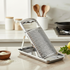 Metal kitchen grater on a marble countertop with lemons and herbs in the background