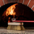 Pizza oven brush in front of a wood fired oven.