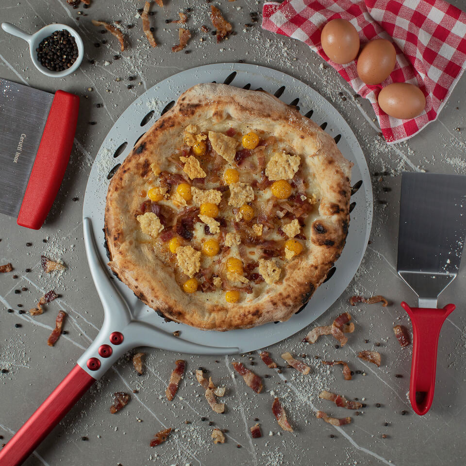 A pizza placed on a Round Perforated Tulip Pizza Peel, next to pizza tools, eggs and a napkin.