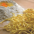 Pile of uncooked spaghetti alla chitarra next to a mound of flour with eggs on a wooden surface