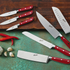 Collection of Berkel Classic Line kitchen knives on a wooden chopping board and blue work surface next to garlic cloves and chillies.