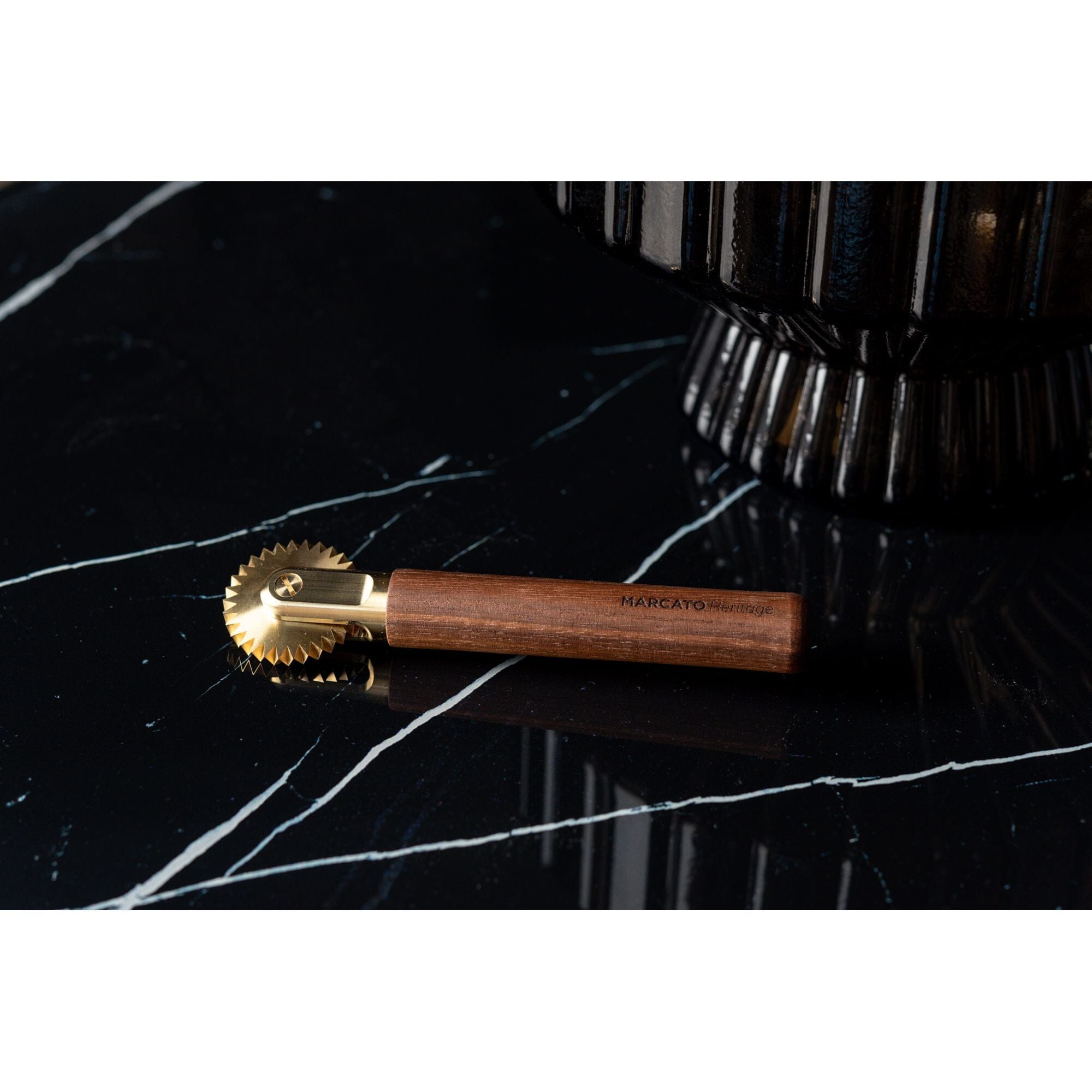 Marcato La Rotella toothed pasta cutter with brass cutting wheel and wooden handle, on a black stone worktop.