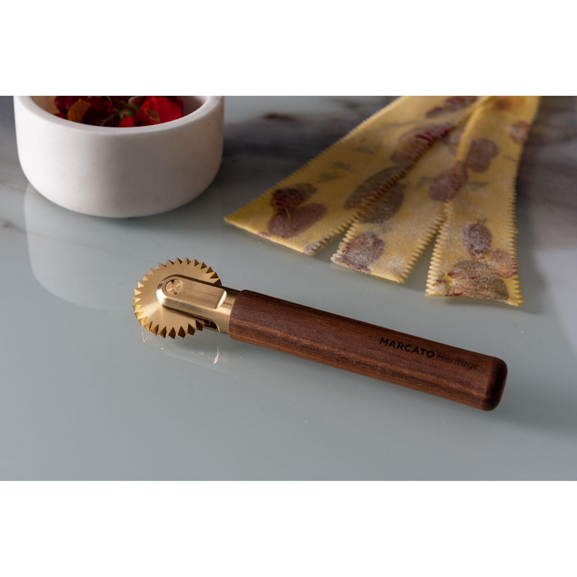 Marcato La Rotella pasta cutter with wooden handle and brass toothed wheel in front of fresh pasta