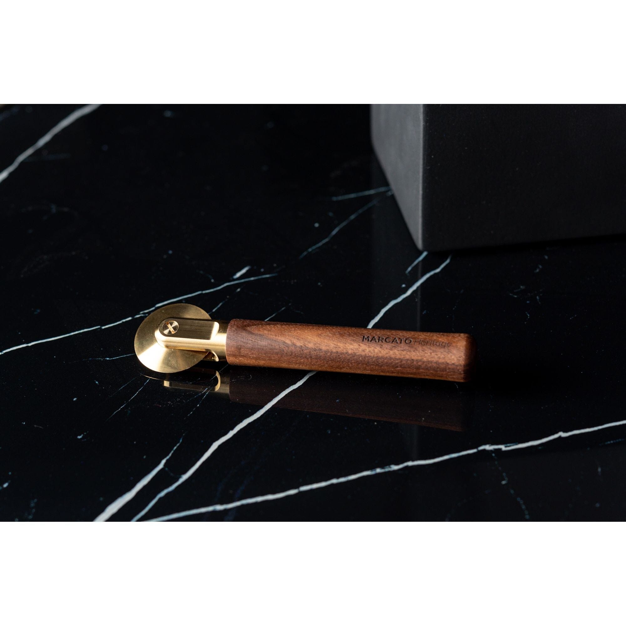 Marcato La Rotella straight pasta cutter with brass cutting wheel and wooden handle, on a black stone worktop.