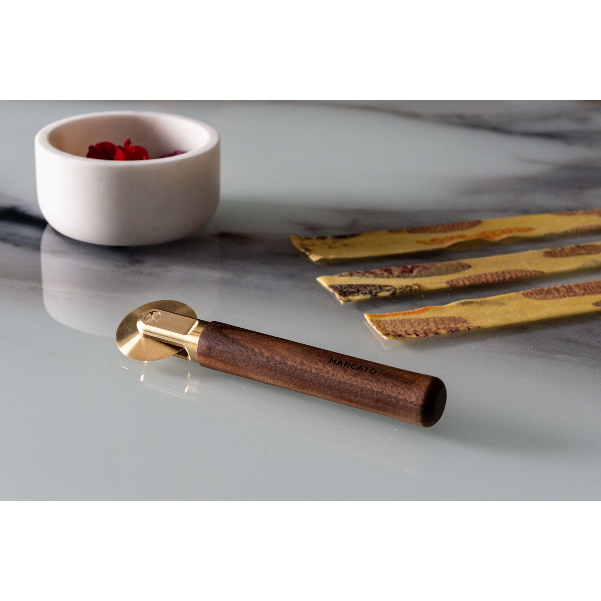 Marcato La Rotella straight pasta cutter with wooden handle and brass toothed wheel in front of fresh pasta