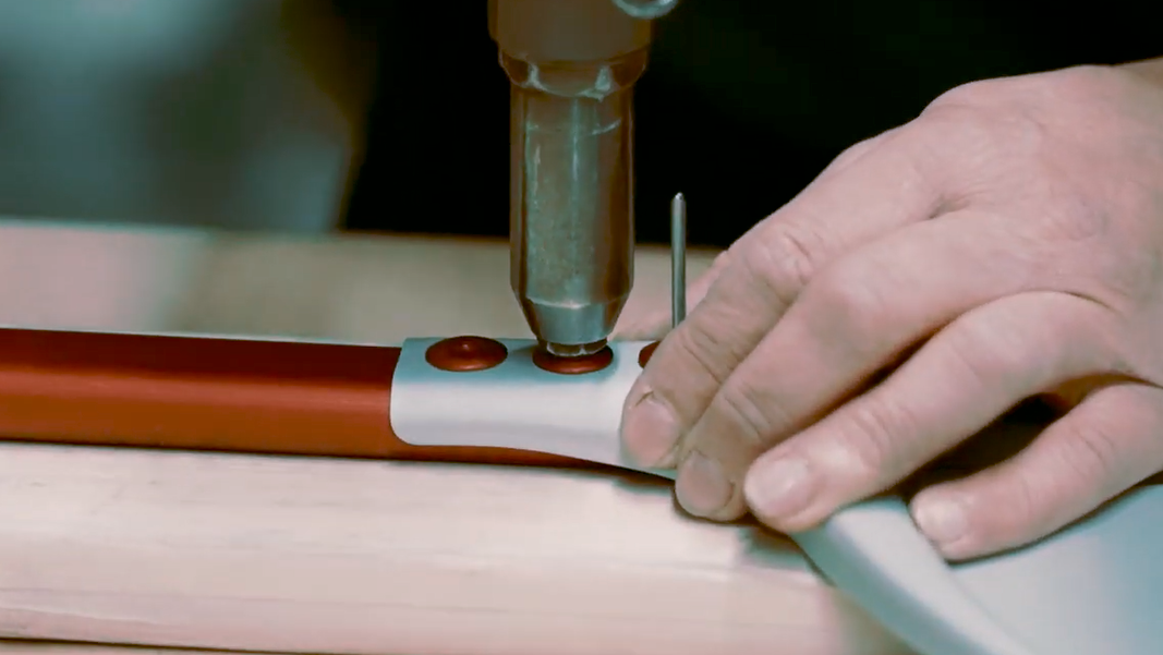 A close-up of a person using a handheld power tool to attach a red and white handle to a Cerutti Inox pizza peel, with the person's hands guiding the fit.