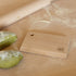 Wooden dough scraper with Marcato logo next to a rolling pin and fresh pasta on a wooden bench