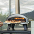 ZiiPa Piana wood fired pizza oven with a pizza being inserted, set against a blurred background.