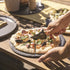 ZiiPa Aquina pizza cutting knife being used on a cooked pizza on a slate serving board on a wooden table top