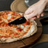Close-up of a ZiiPa Aquina pizza cutting knife being used on a cooked pizza on a wooden serving board