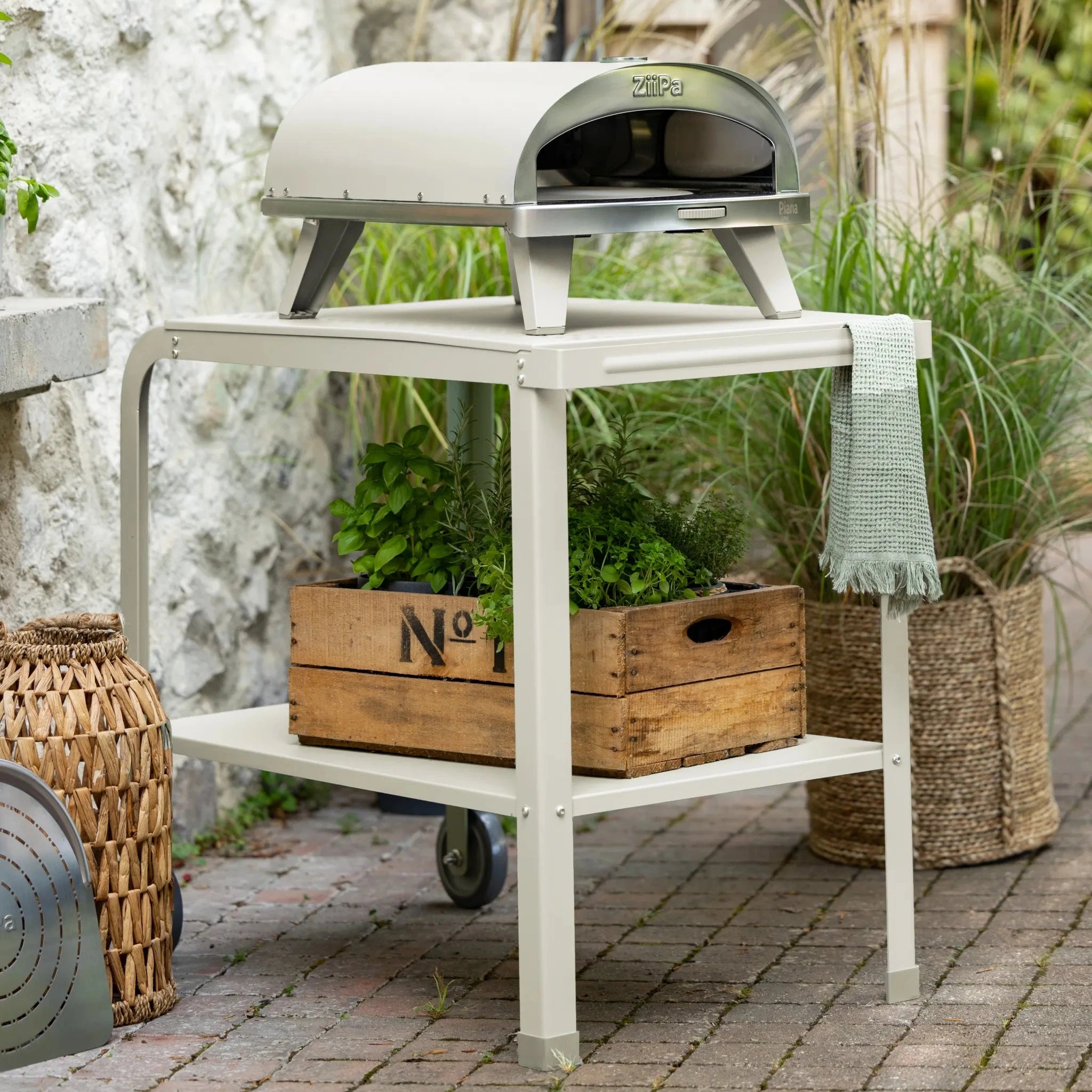 ZiiPa Piana wood-fired pizza oven on a vallone trolley, both in Chalk colour, on a garden patio