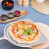 ZiiPa Aquila perforated pizza peel with a beech wood handle with a cooked pizza on a blue worktop from a side angle