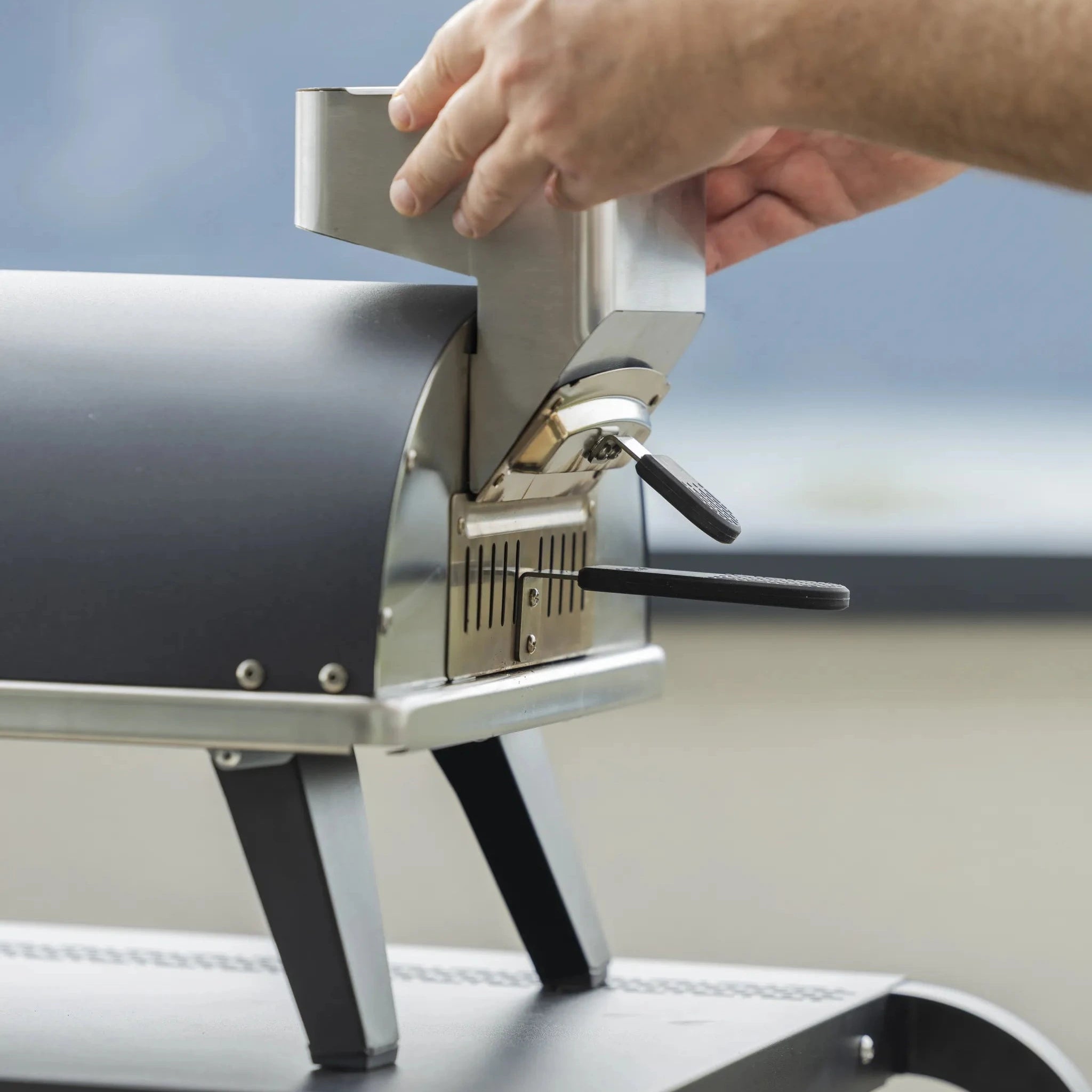 A person attaching a Donato pellet dispenser to the rear of a Piana Pizza Oven