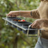 Person carrying Tellini topping station with tomatoes inside in an outdoor environment