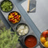 Top down view of a Tellini topping station with herbs, tomatoes, mozzarella and tomato sauce inside the charcoal spetina dough boxes