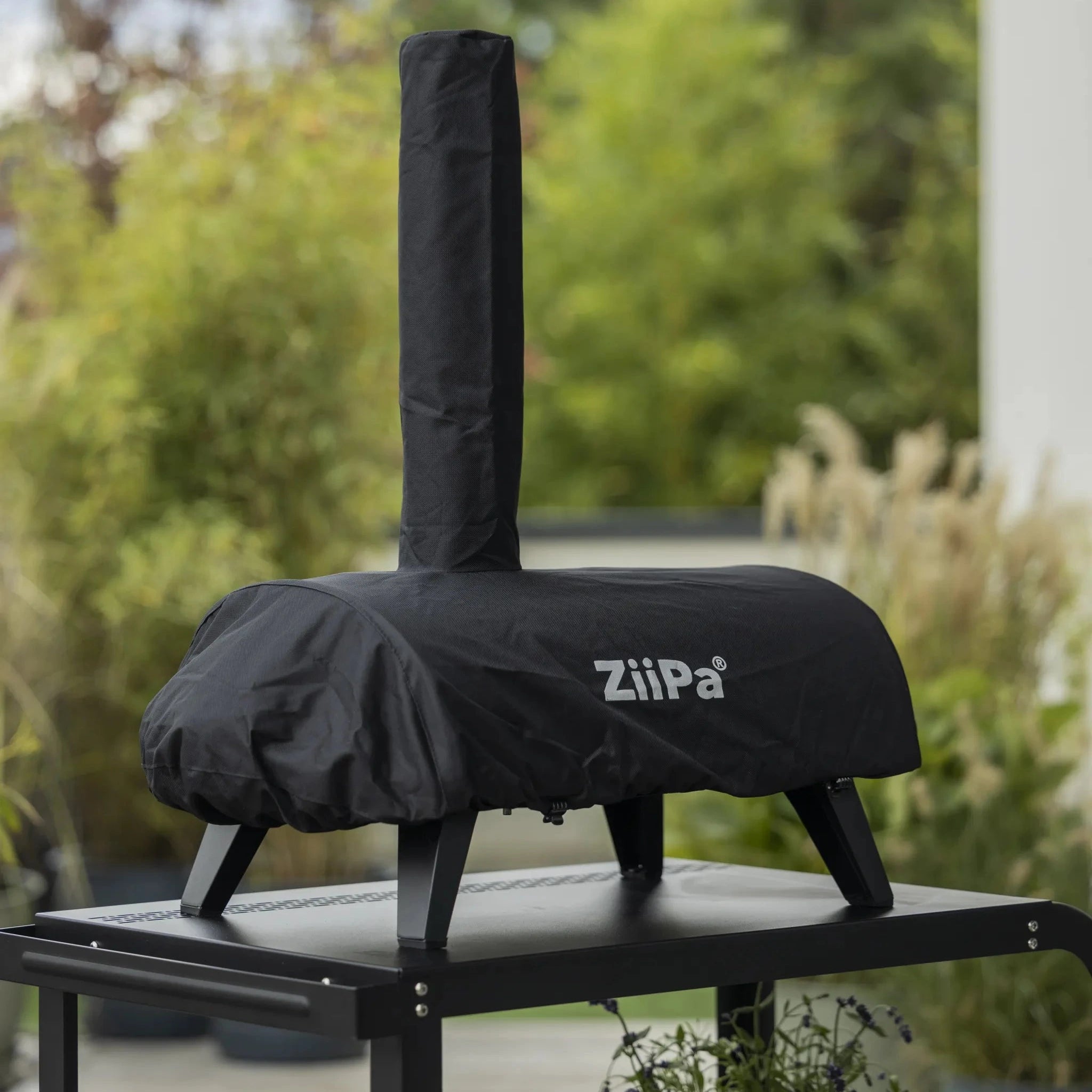 ZiiPa Piana pizza oven in a Sacco protective cover on a Vallone pizza oven trolley in a green, outdoor setting