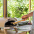 ZiiPa Ranella pizza stone brush being inserted into ZiiPa Piana wood pellet pizza oven to clean cordierite stone