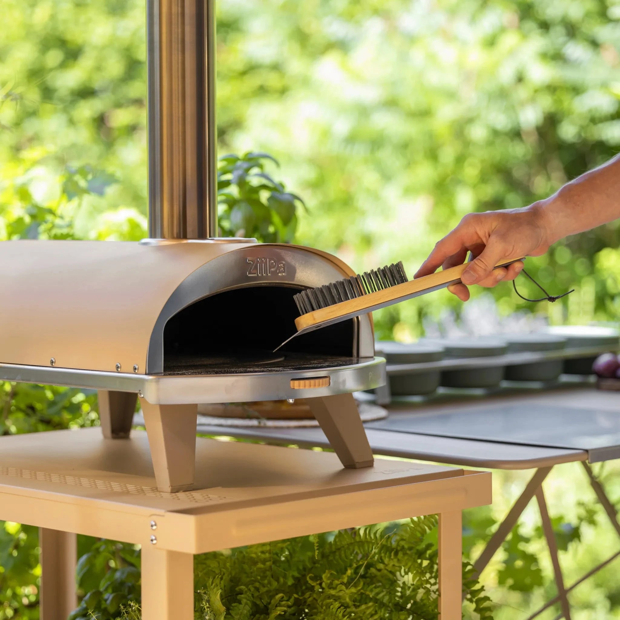 ZiiPa Ranella pizza stone brush in use on ZiiPa Piana cordierite stone showing compact length suited to small oven mouth