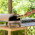 ZiiPa Ranella pizza stone brush in use on ZiiPa Piana cordierite stone showing compact length suited to small oven mouth