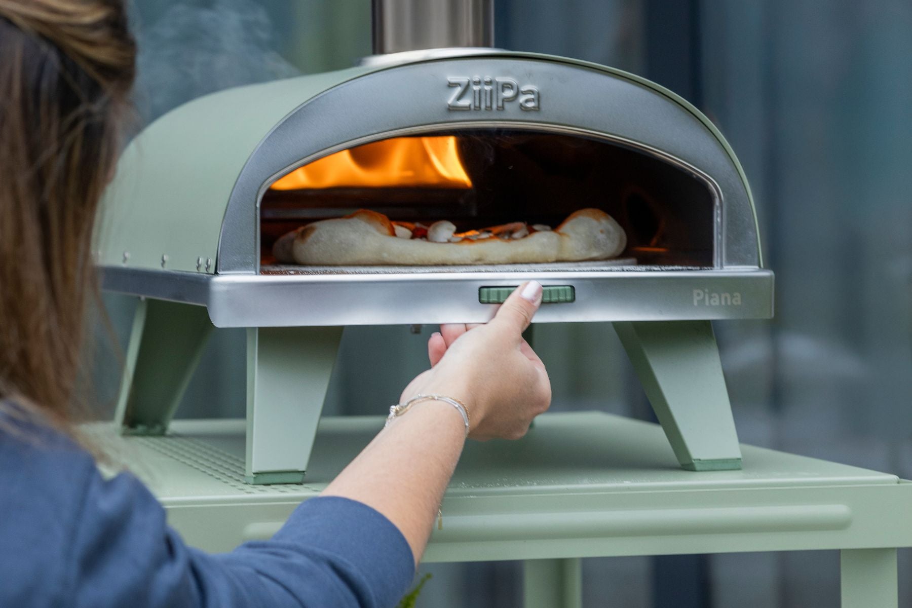 ZiiPa Piana wood-fired pizza oven in Eucalyptus in use outdoors with chef using the rotating dial for the internal pizza stone