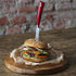Red elegance steak knife pushed through a cheeseburger on parchment paper and a wooden board.