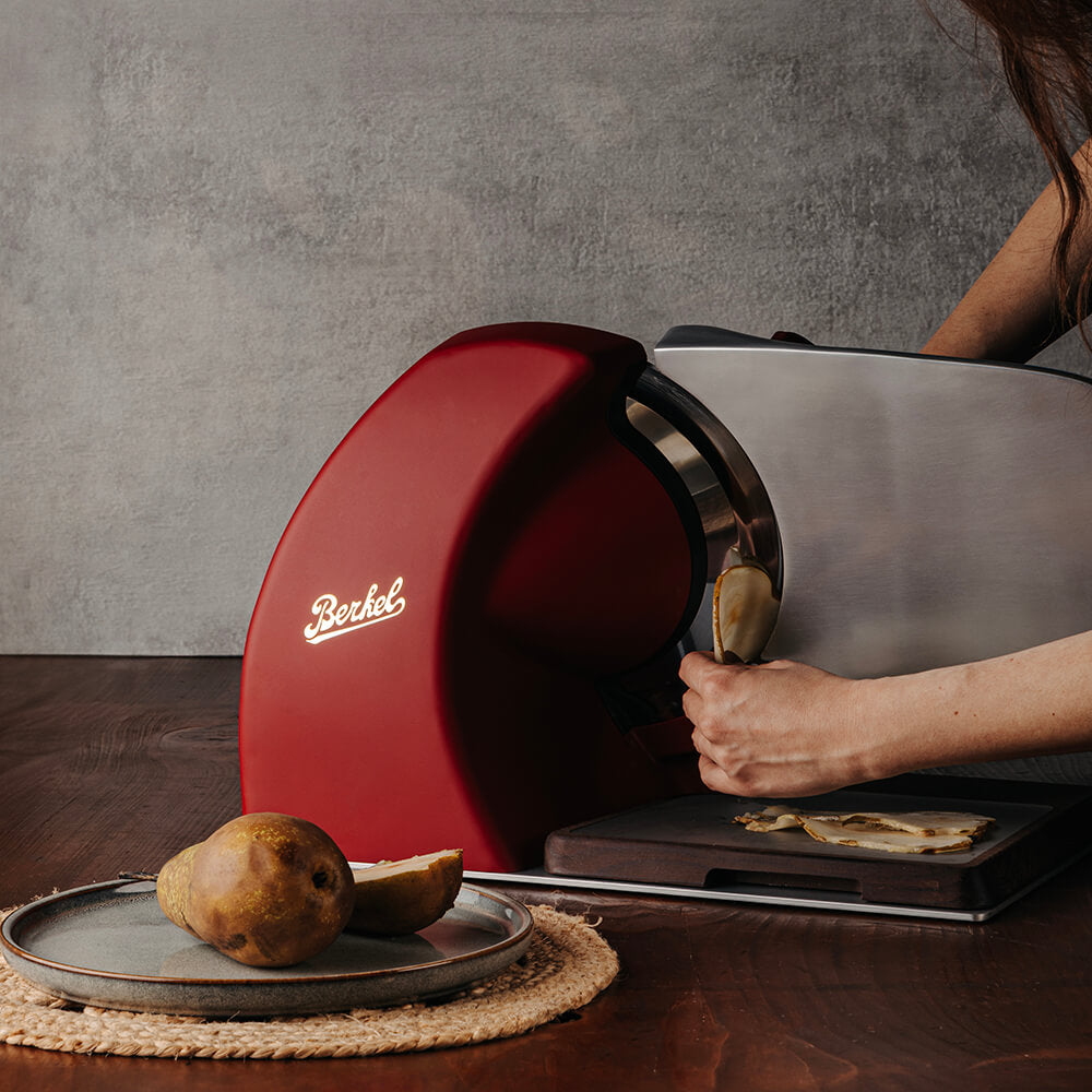 Berkel Home Line Plus 250 Food Slicer with 250mm blade in matte red slicing cheese on a wooden kitchen counter, ideal for home gourmet use.