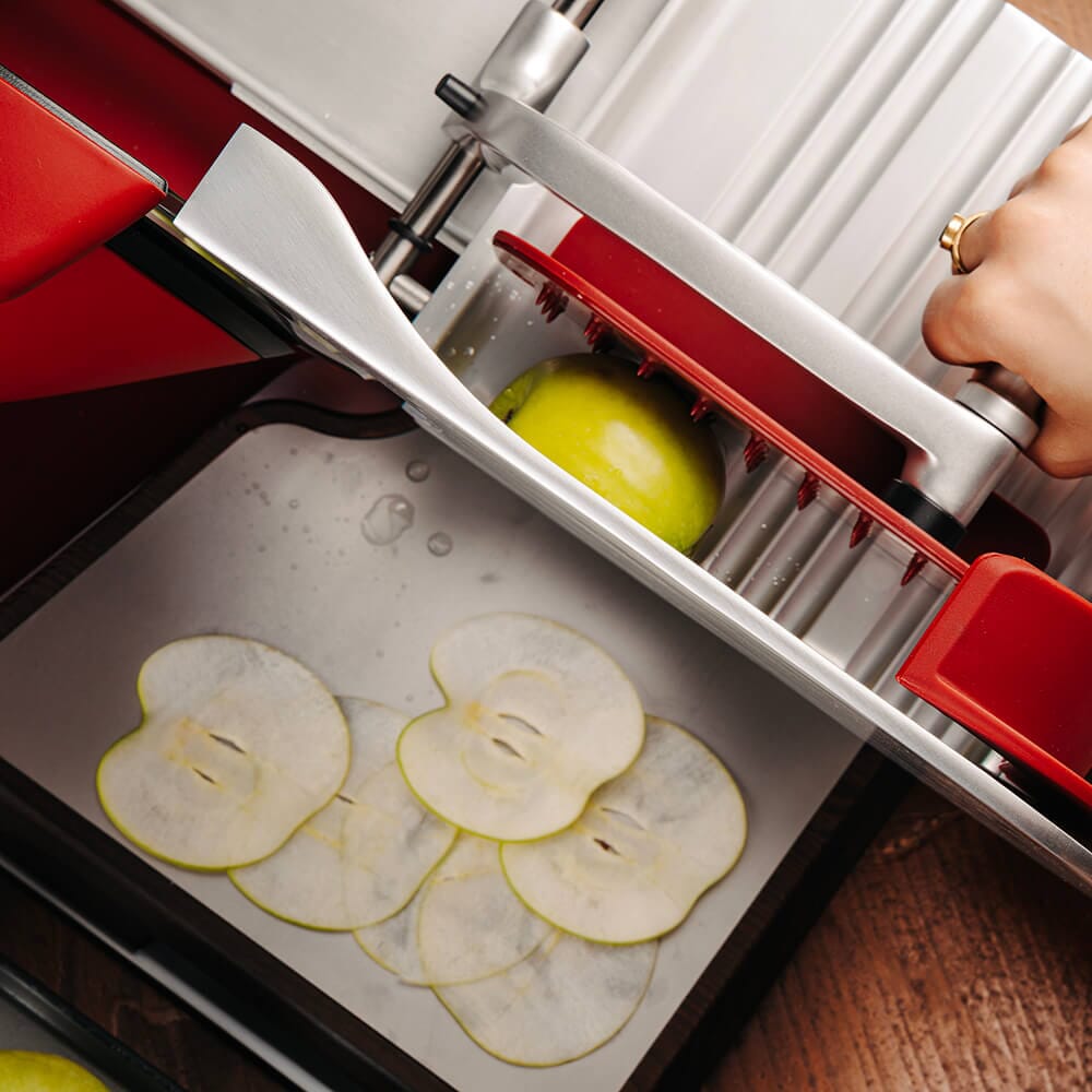 Berkel Home Line Plus 250 Matt Red slicer slicing apple on a Home Line Plus slicer cutting board underneath