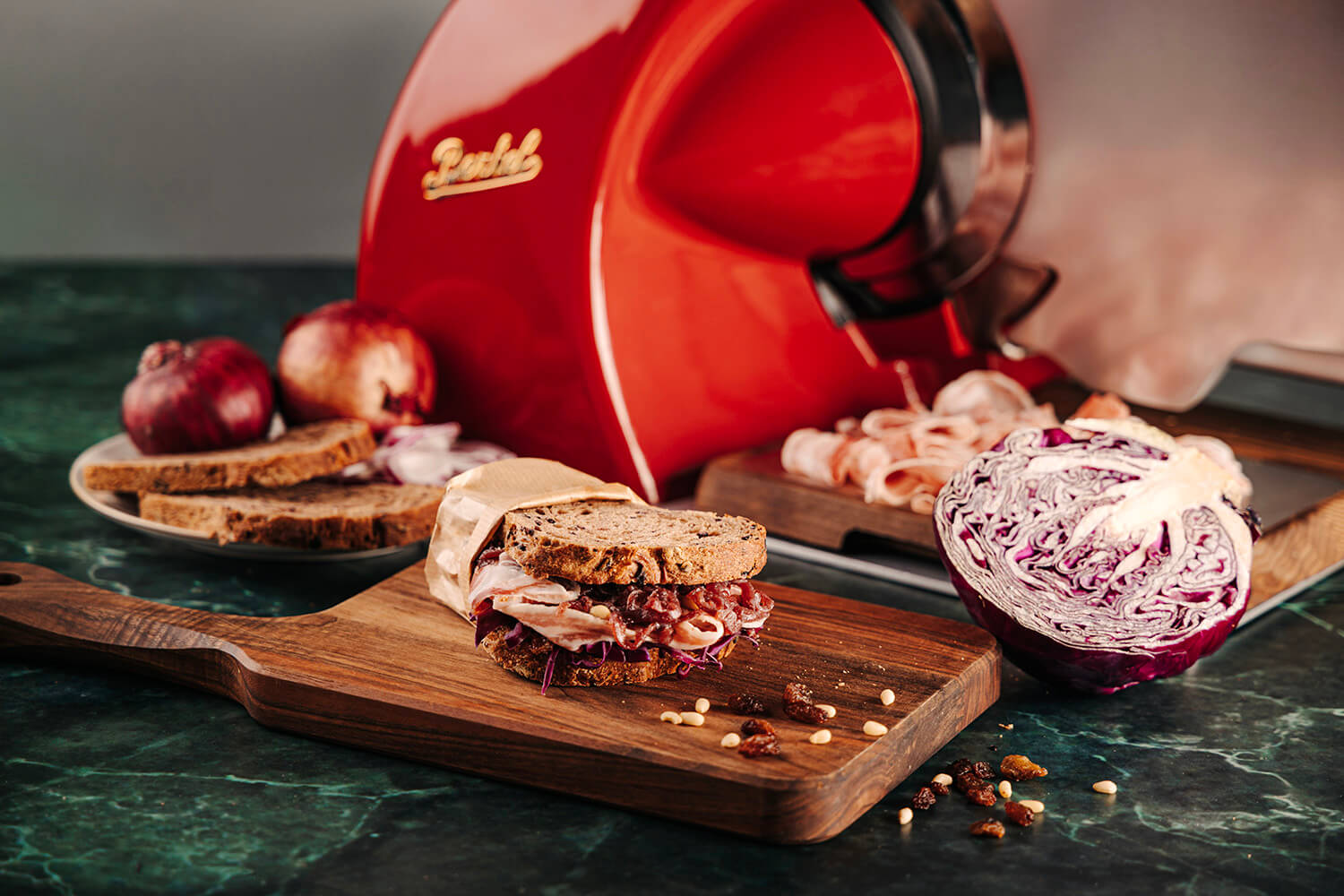 Red kitchen slicer on a marble surface with food items and a cutting board.