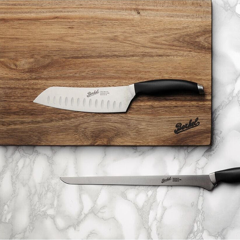 Berkel Teknika knives with a Berkel acacia cutting board, on top of a marble work surface.