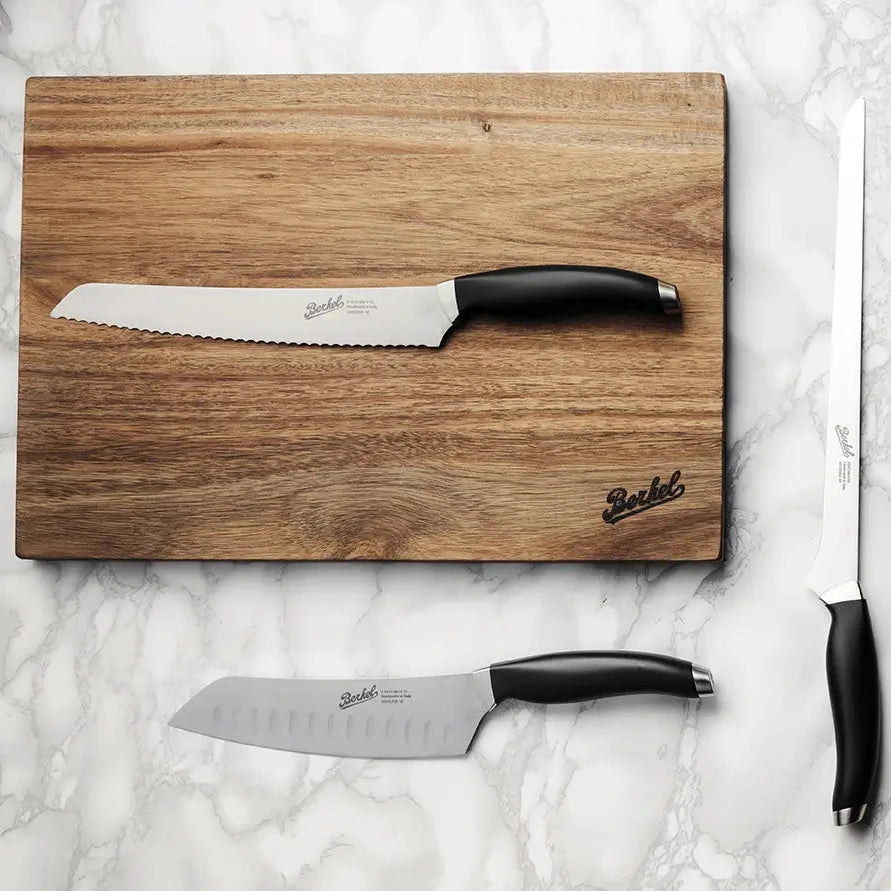 Berkel Teknika knives with a Berkel acacia cutting board, on top of a marble work surface.
